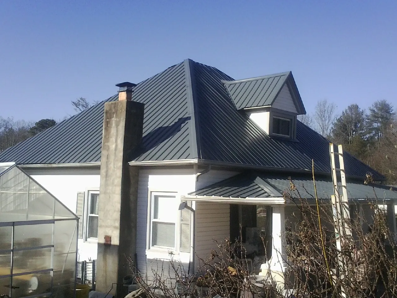 Dark blue standing seam metal roof on a white farmhouse with dormer — Slate & Tile Roof Repair by Roofing Brothers in Longs