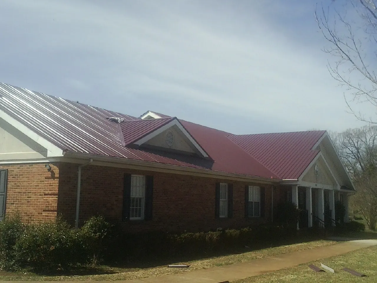 Red metal roof with gabled entries on a long brick building, from a Hail Damage Roof Repair job in Longs