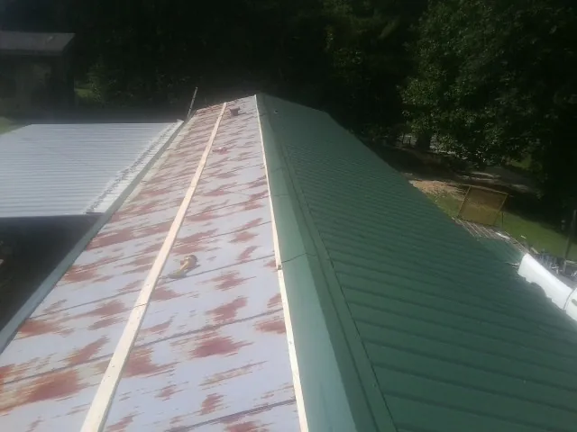 Old rusted panels beside newly installed green metal roofing — Wind Damage Roof Repair by Roofing Brothers in Longs