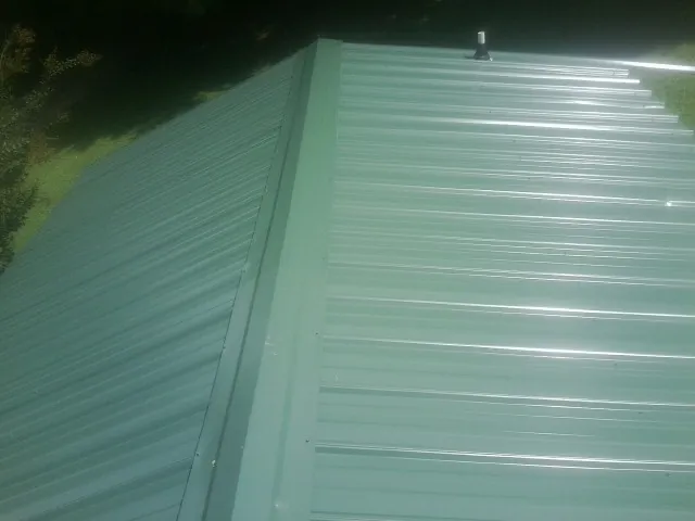 New green metal panels meeting at the ridge of a roof — Flat Roof Repair work by our crew in Longs