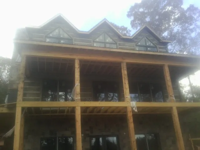 Dormers and porch framing on a large log home under construction — Roof Coating work by our crew in Longs