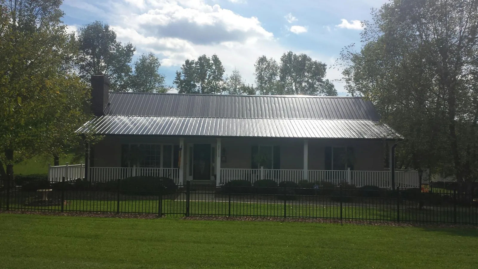 Gray metal roof on a brick ranch with a full width front porch — Gutter Guard Installation work by our crew in Longs