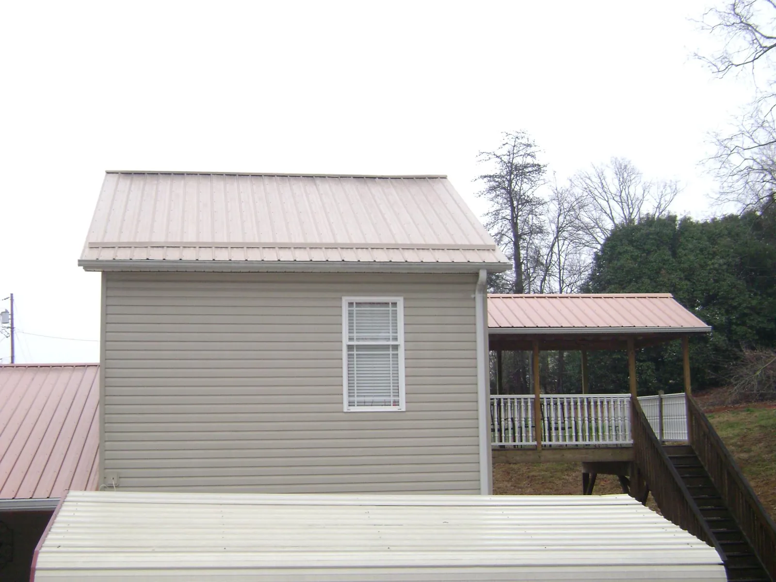 Tan metal roofs on a two story addition and attached porch, from a Roof Replacement job in Longs